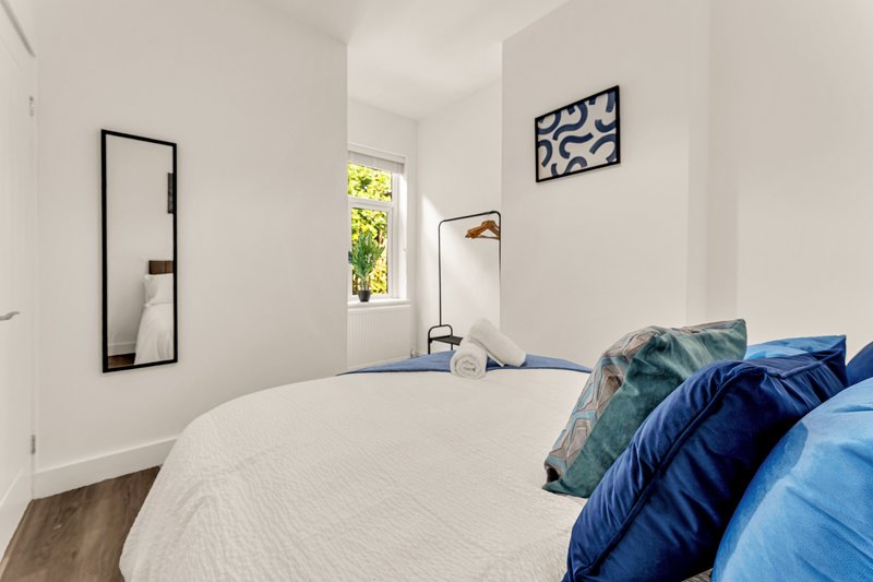 Bright bedroom with double bed, blue bedding, wall mirror, and framed artwork