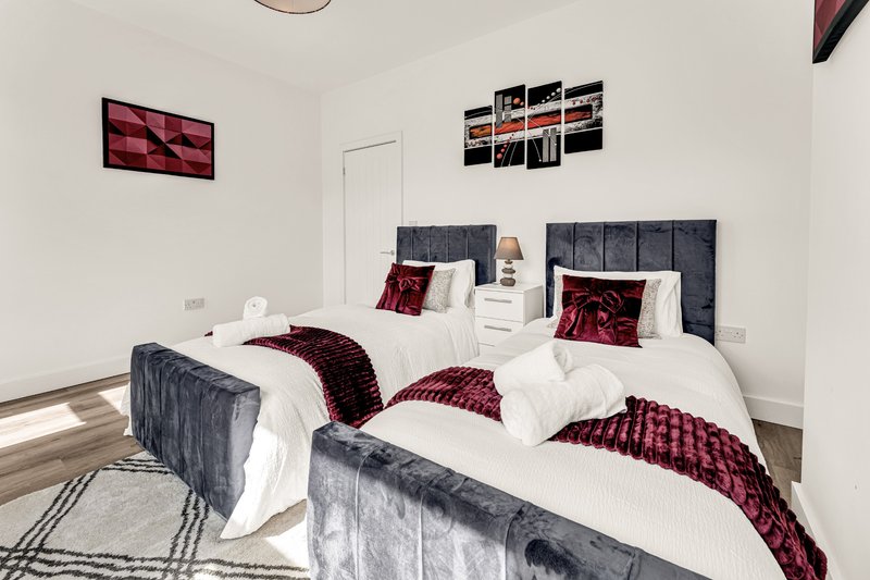 Modern bedroom with two single beds, burgundy bedding, gray upholstered headboards, and wall art