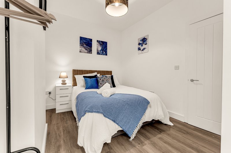 Bright bedroom with double bed, blue bedding, white nightstand, framed wall art, wooden flooring