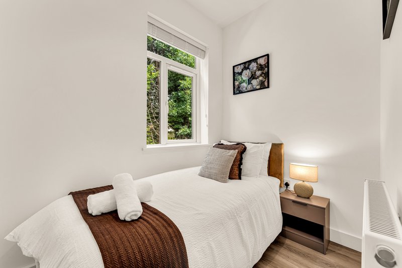 Bright bedroom with single bed, wooden headboard, bedside table and window with garden view
