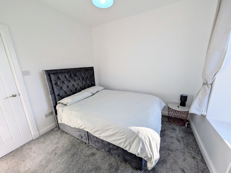 Bedroom with black upholstered bed, white bedding, grey carpet and white walls