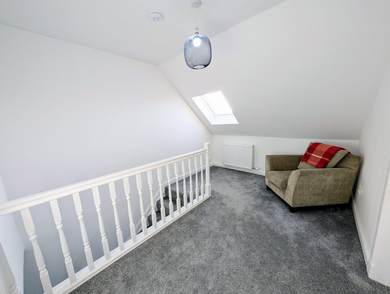 Attic bedroom with white crib, armchair, skylight window and grey carpet