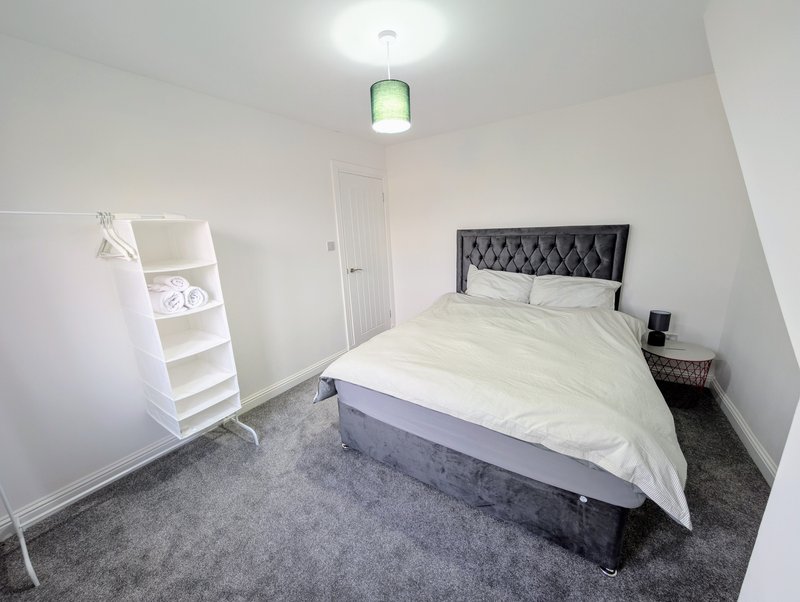 Bedroom with double bed, black headboard, white shelving unit, grey carpet and pendant light