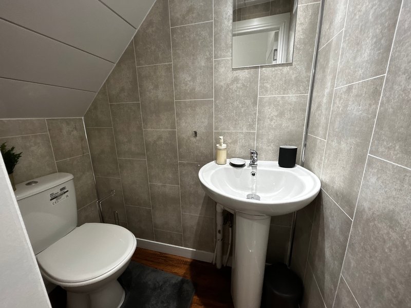 Modern bathroom with toilet, pedestal sink, mirror and tiled walls under sloped ceiling
