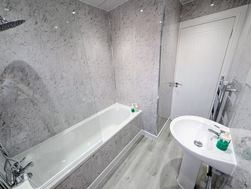 Modern bathroom with marble-effect tiles, white bathtub, pedestal sink and shower enclosure