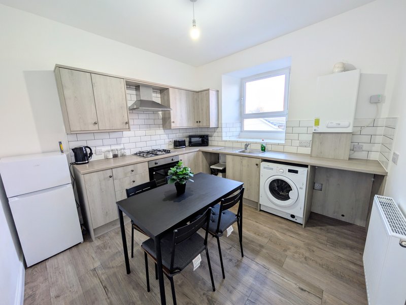 Kitchen with cream cabinetry, black dining table, white appliances and subway tile backsplash