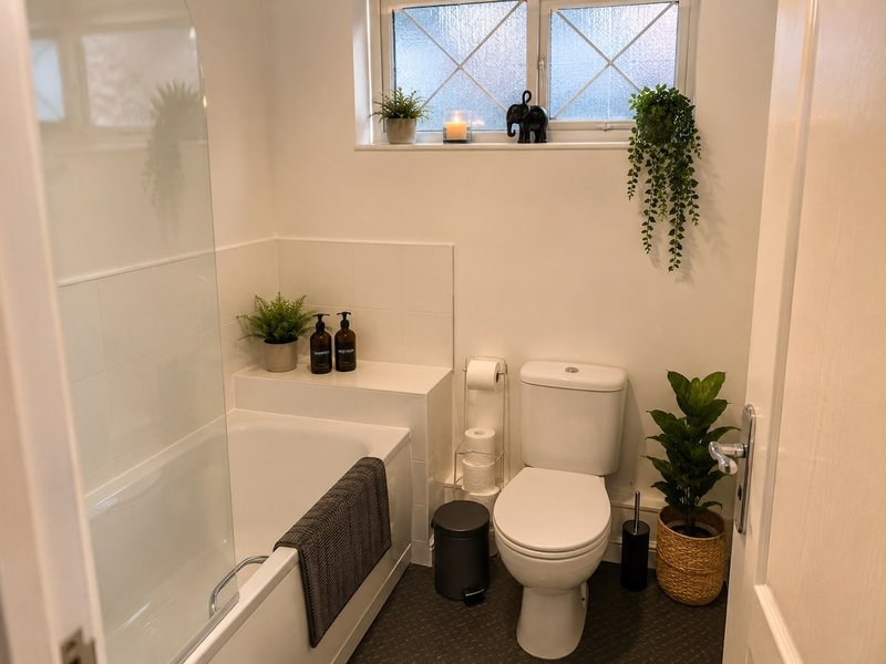 Clean bathroom with toilet, sink, shower enclosure, plants and window