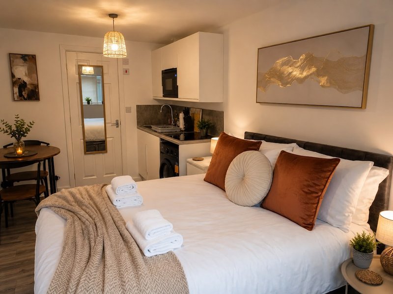 Bedroom with double bed, rolled towels, decorative pillows, kitchenette, and framed artwork