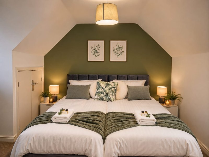Bedroom with two single beds, green feature wall, pendant light, and botanical wall art