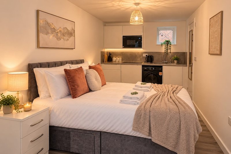 Studio bedroom with double bed, kitchenette, pendant light and warm neutral decor