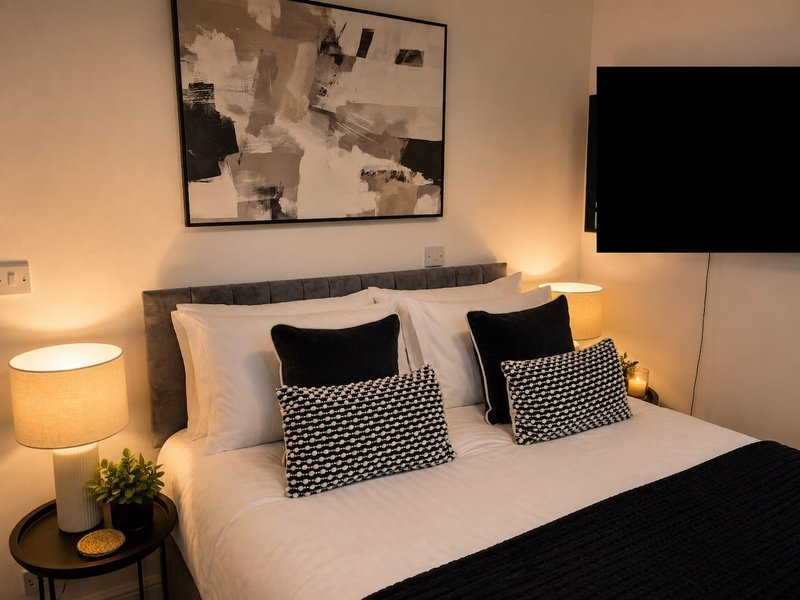 Modern bedroom with double bed, black and white patterned cushions, bedside lamps and wall art