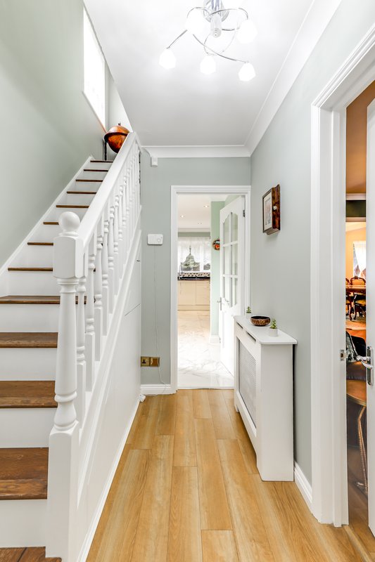 Bright hallway with wooden staircase, white railings, and light wood flooring