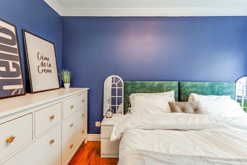 Modern bedroom with blue walls, white bed, cream dresser and wooden floor