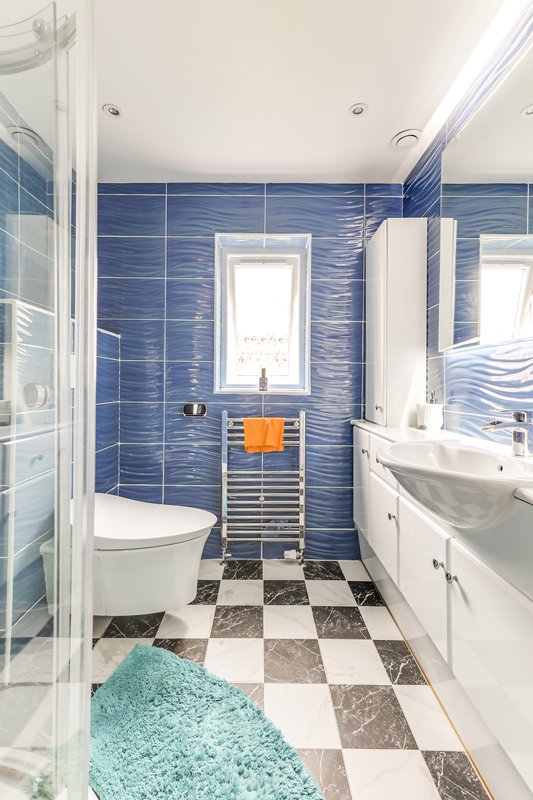 Modern bathroom with blue tile walls, white fixtures, checkered floor and turquoise bath mat