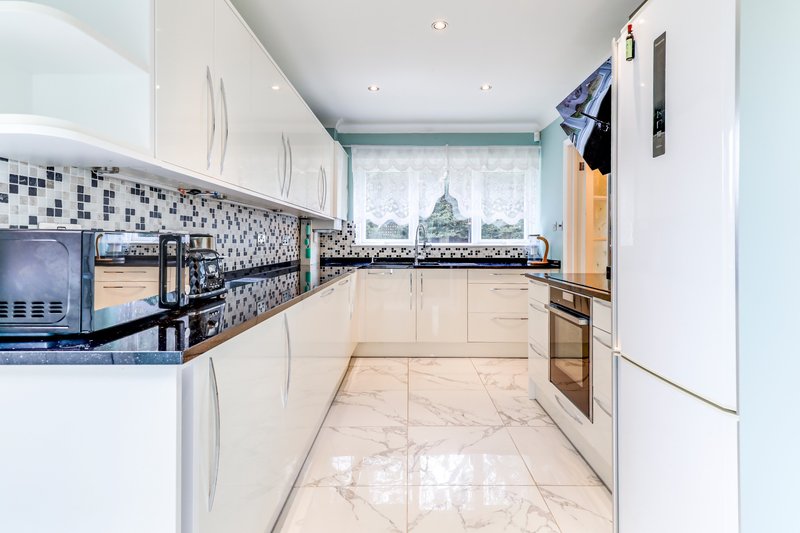 Modern kitchen with white cabinetry, black granite countertop, mosaic backsplash and marble flooring