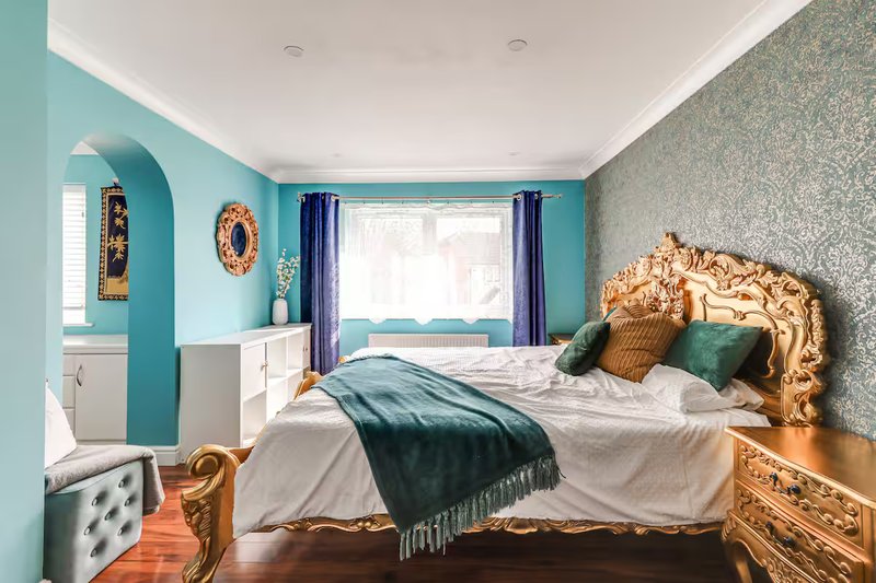 Bedroom with turquoise walls, gold bed frame, white bedding, and dark blue curtains
