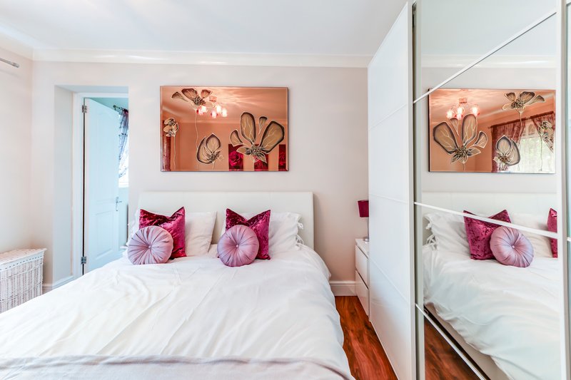 Modern bedroom with double bed, pink velvet cushions, mirrored wardrobe and wall art