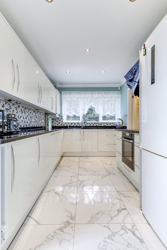Modern galley kitchen with white cabinetry, marble flooring, black mosaic backsplash and window