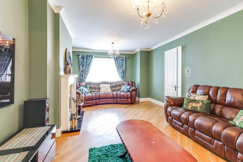 Spacious living room with leather sofas, wooden floor, green walls and bay window
