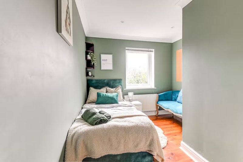 Bedroom with single bed, green headboard, shelving, and armchair by window
