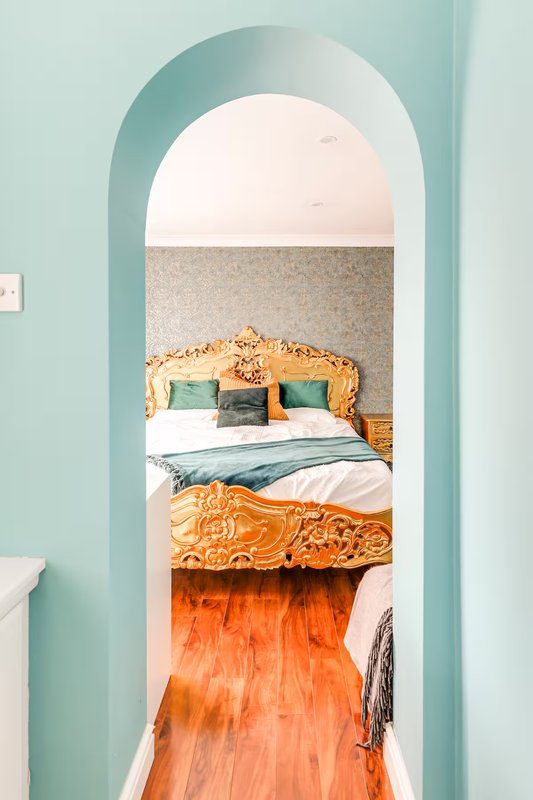 Bedroom with ornate gold headboard, green and white bedding, viewed through mint-green arched doorway