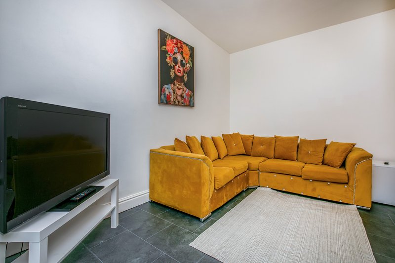 Living room with mustard yellow corner sofa, flat-screen TV, and framed floral artwork on wall