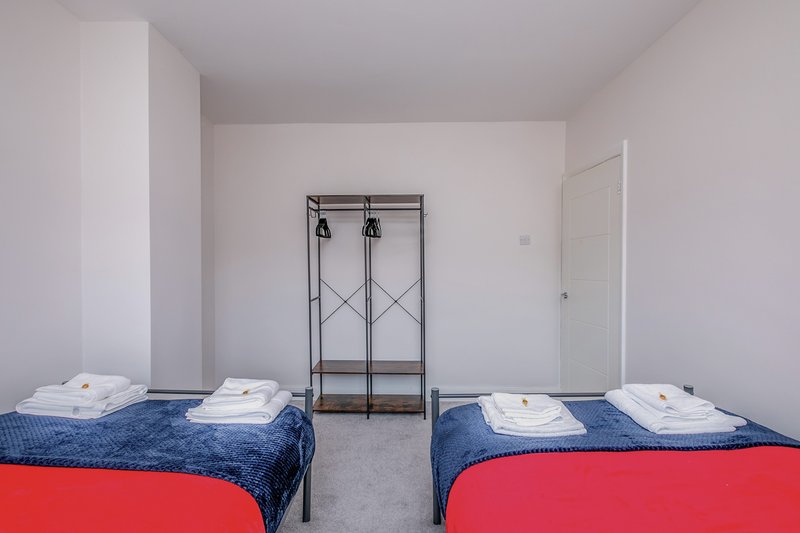 Bright twin bedroom with two beds, coat rack, and neutral walls and flooring