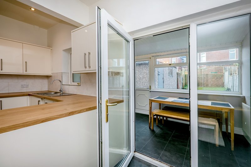 Modern kitchen with cream cabinets, wooden countertop, and glass doors opening to dining area