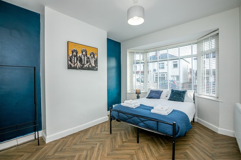 Bright bedroom with double bed, blue accent wall, framed artwork and large windows