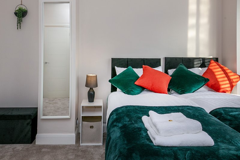 Bedroom with green upholstered bed, colorful cushions, white bedding, and hanging plant decor