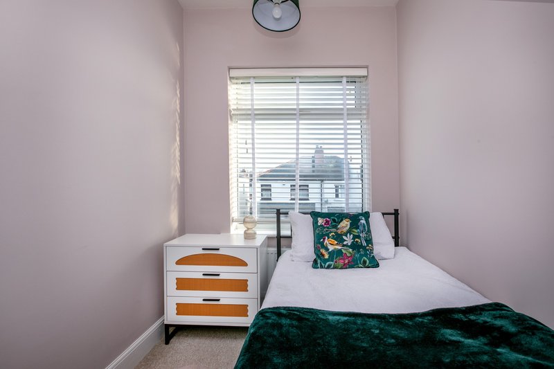 Compact bedroom with single bed, white dresser with orange drawers, patterned cushion, and window with shutters