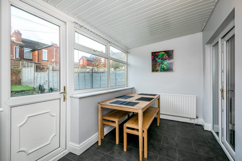Bright sunroom with wooden dining table, chairs, dark tile flooring and garden view