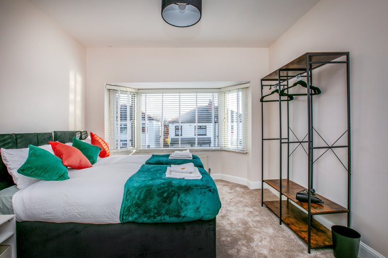 Bright modern bedroom with double bed, colorful pillows, turquoise throw, and metal clothing rack