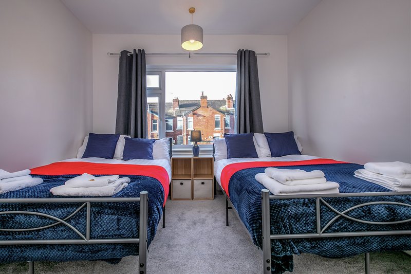 Twin bedroom with two single beds, red and blue bedding, window overlooking street