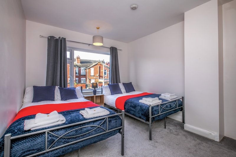 Bright bedroom with two single beds, red bedding, window with city view, and pendant light