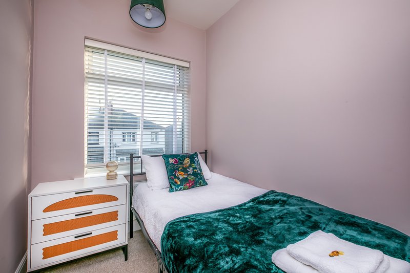 Compact bedroom with single bed, orange and white dresser, window with blinds, pink walls