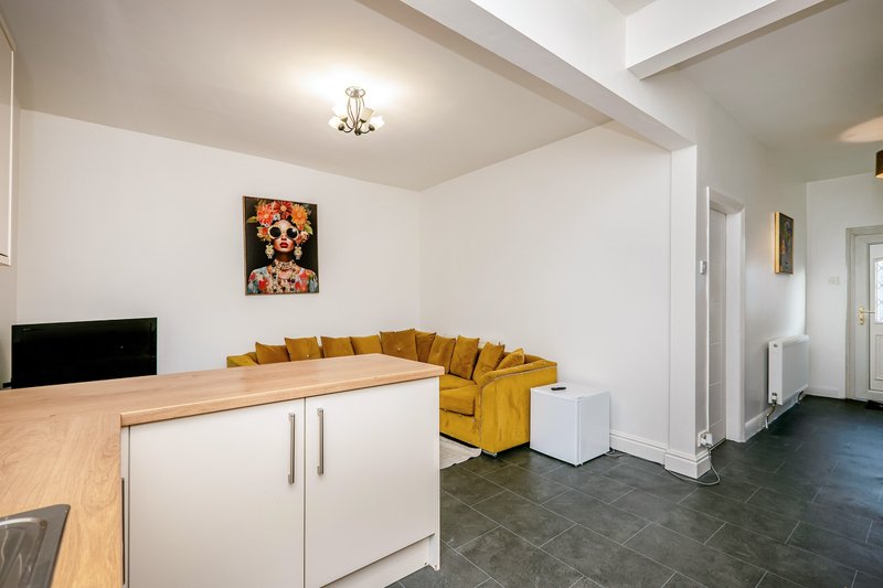 Open-plan kitchen and living area with mustard yellow sofa, wooden countertop, and artwork on wall