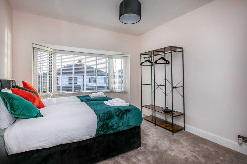 Bright bedroom with double bed, green velvet bedding, large window and metal shelving unit