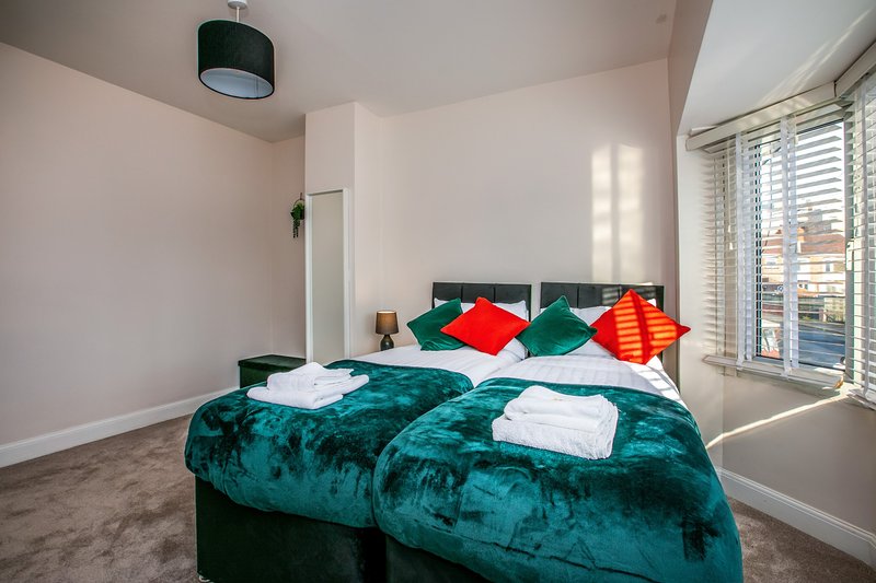 Bright bedroom with teal velvet bed, colorful cushions, white towels and glass doors to balcony