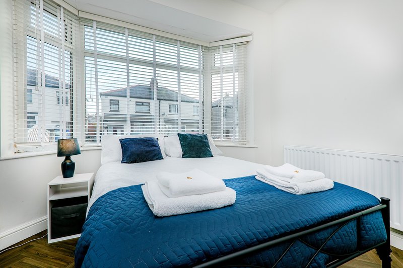 Modern bedroom with blue bed, white pillows, nightstand and large window overlooking city