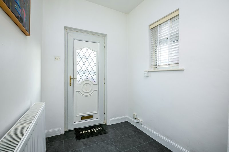 Bright entryway with white door, dark tile floor, radiator and window with shutters