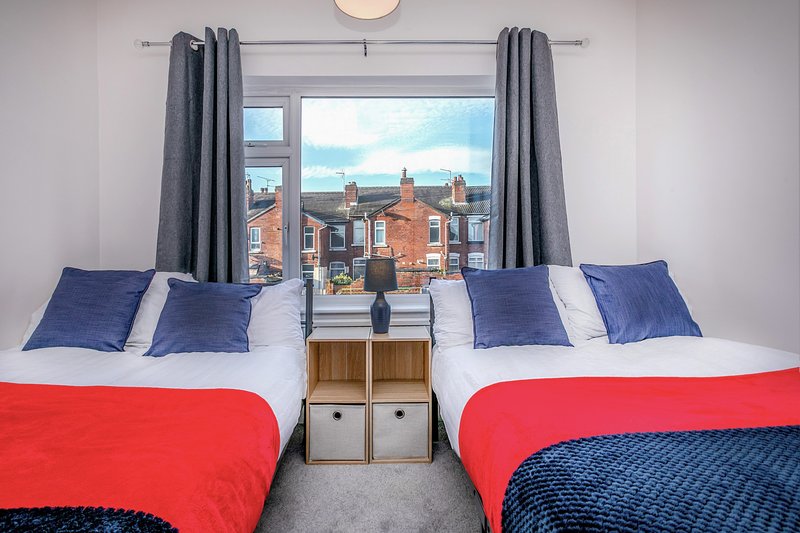 Twin bedroom with red and blue bedding, large window overlooking brick buildings