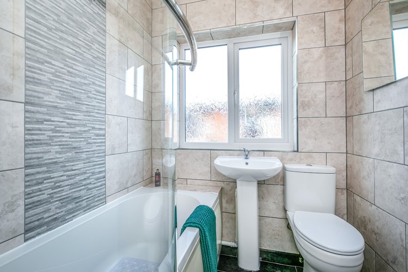 Bathroom with bathtub, pedestal sink, toilet, tiled walls and window