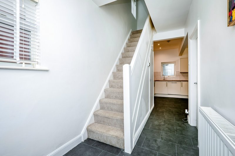 Hallway with staircase, white railing, tiled floor, and doorway to kitchen area