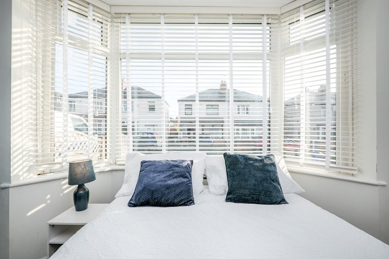 Bright bedroom with double bed, blue cushions, white shutters and city views