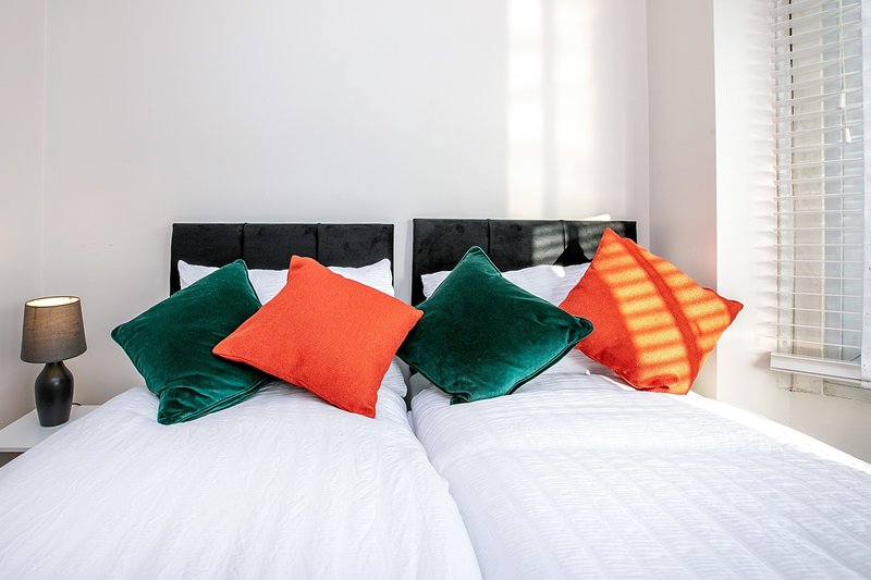 Bright bedroom with double bed, colorful cushions, black headboard, and bedside lamp.