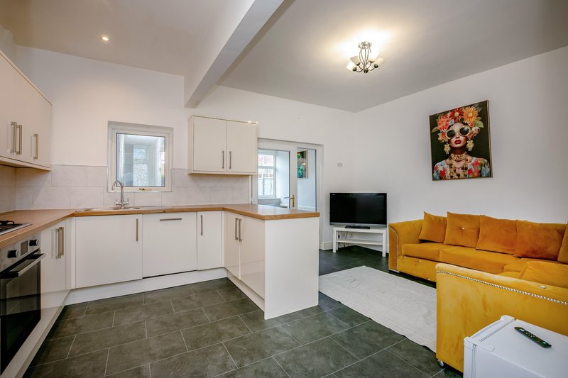 Open-plan kitchen and living area with white cabinetry, yellow sofa, and wall art