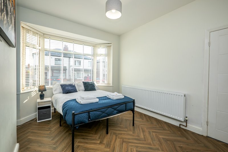 Bright bedroom with blue bed, herringbone floor, bay window and radiator
