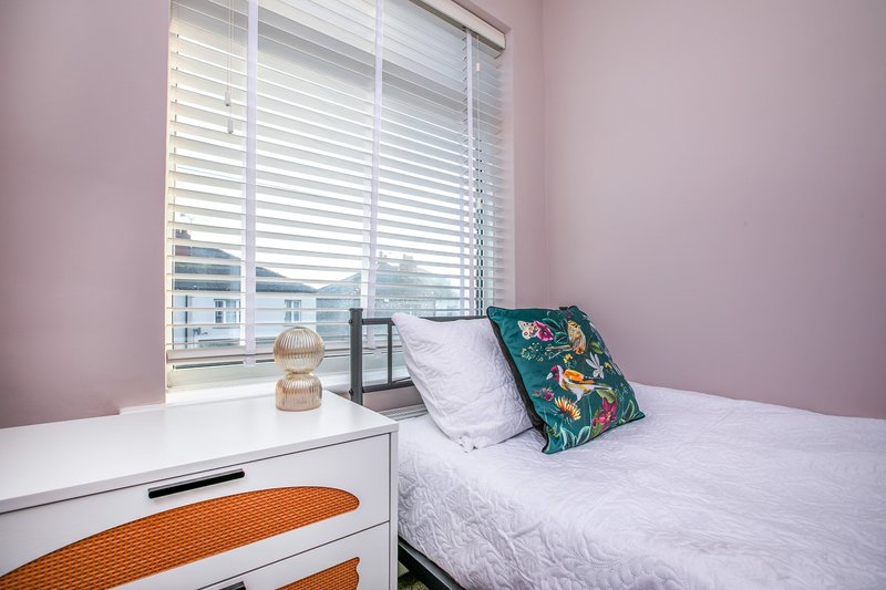 Pink bedroom with single bed, white nightstand, decorative cushions and shuttered window