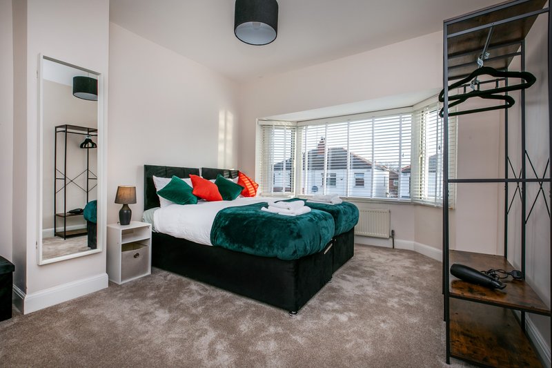 Spacious bedroom with double bed, green velvet bedding, colorful pillows, large windows and carpeted floor